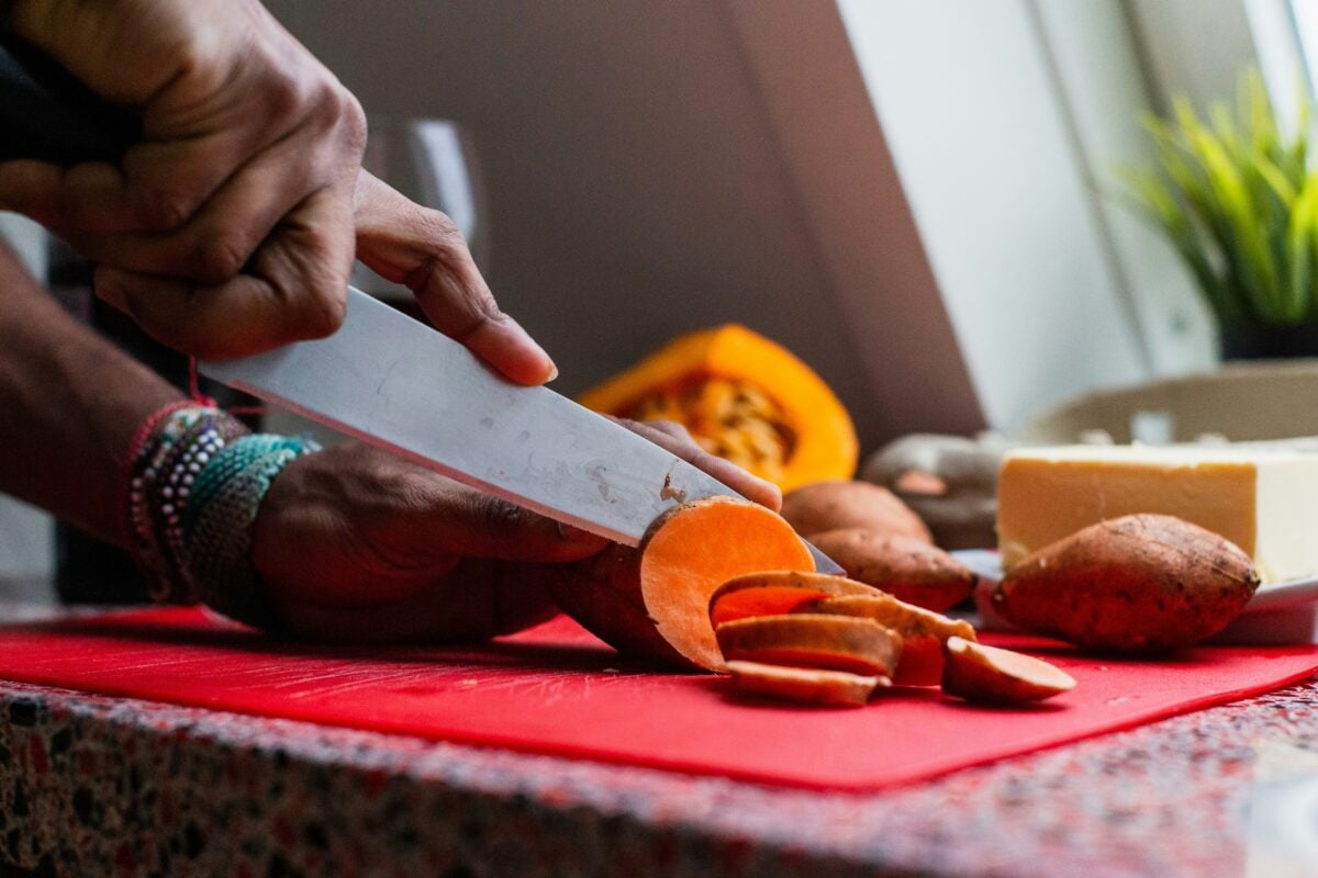 Hands using a knife to slice sweet potatoes into disks.