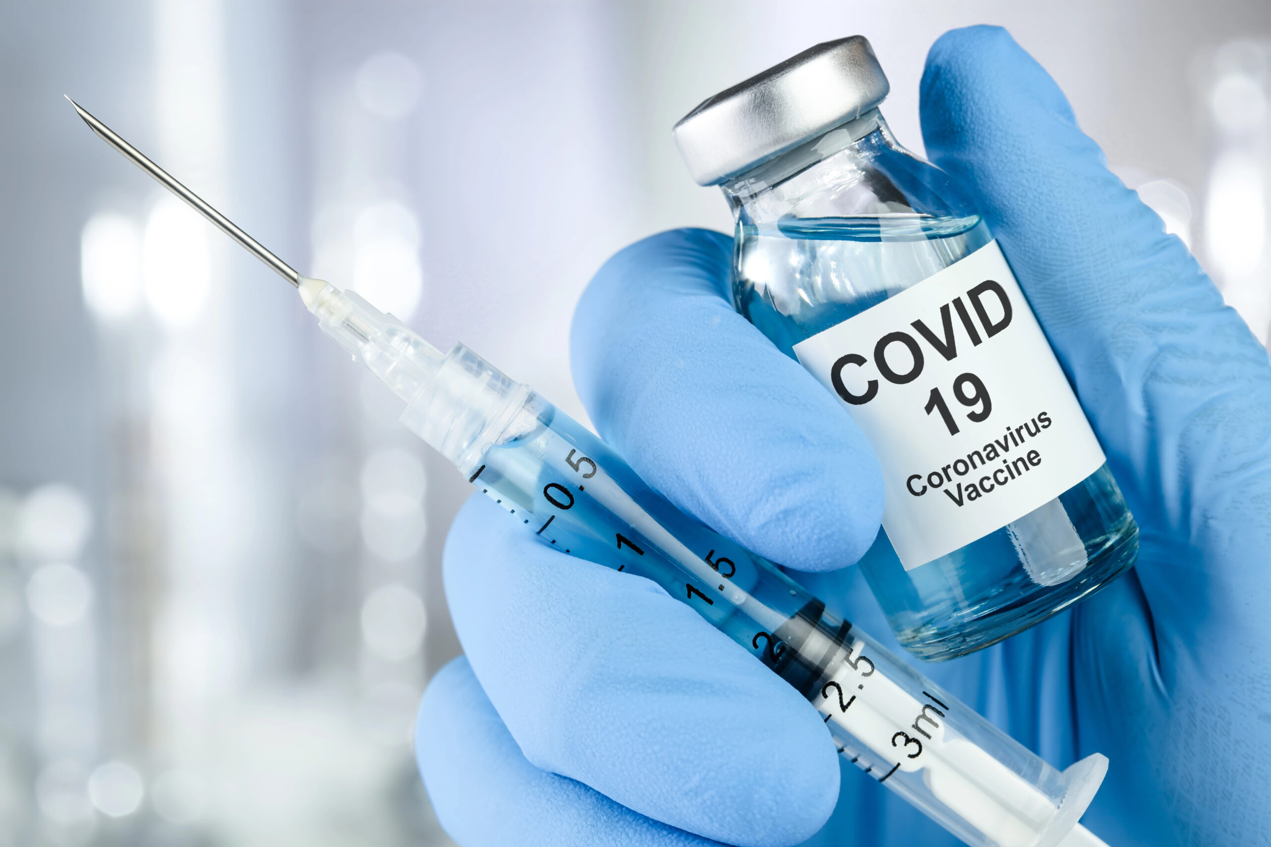 Gloved hand holding a vial and shot of Covid-19 vaccine.