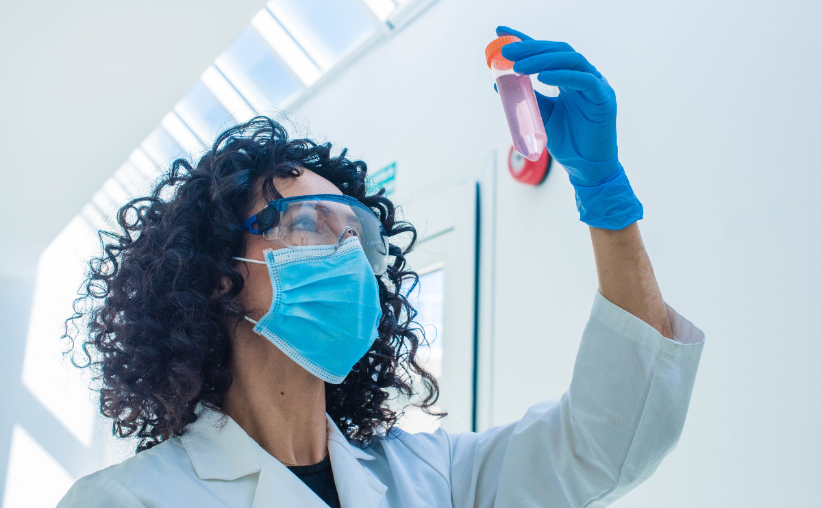 A female scientists with mask on holding up a test tube.