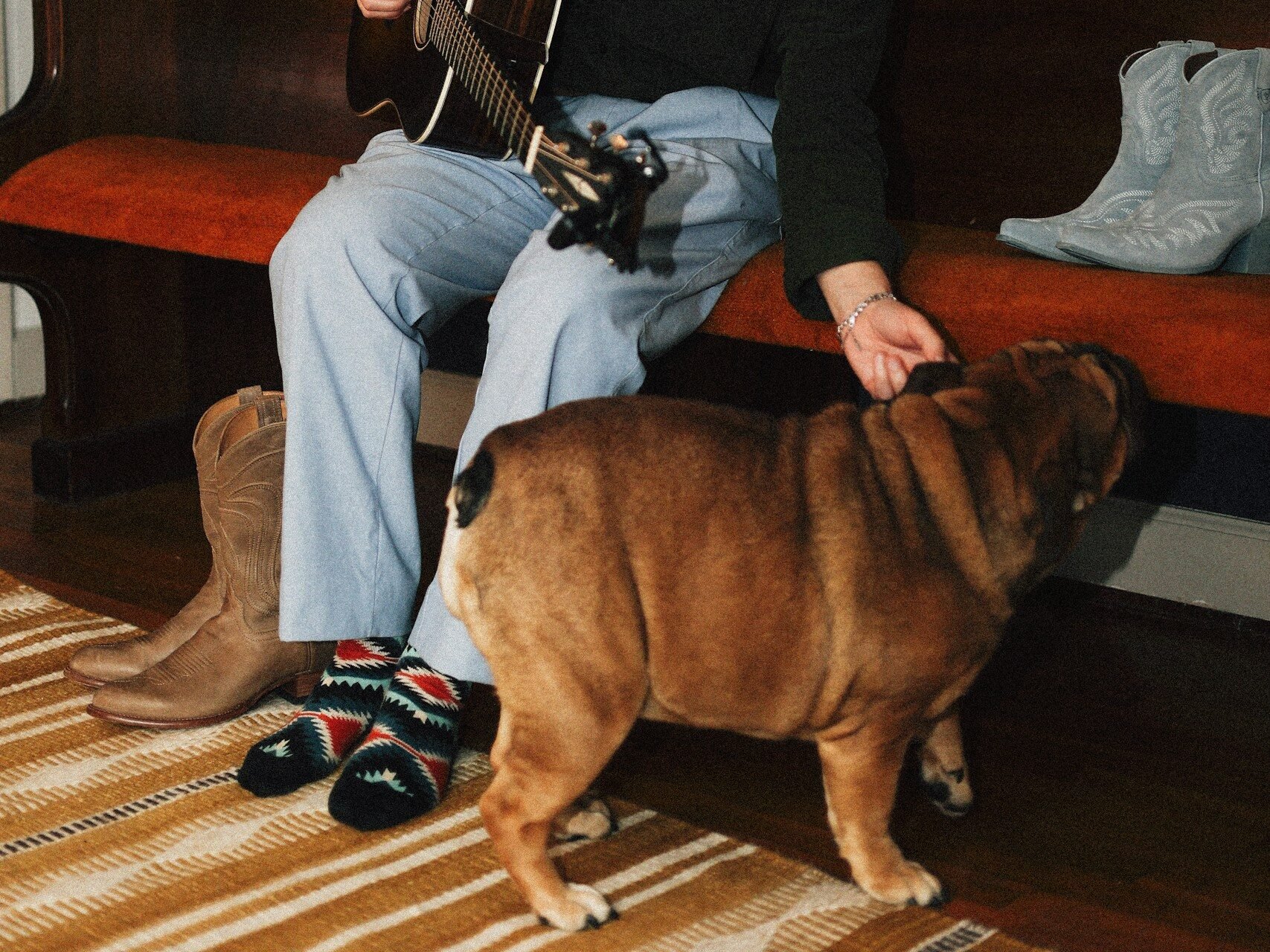 Person playing guitar on church pew with cowboy boots and Bulldog.