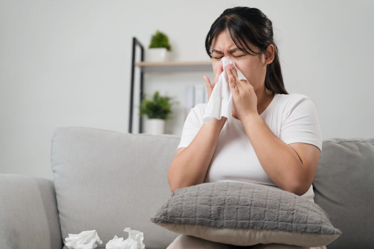 Young woman got a nose allergy sneezing sitting on the sofa at home. Flu, Influenza, Sick, Fever, Illness. Healthcare and medical concept.