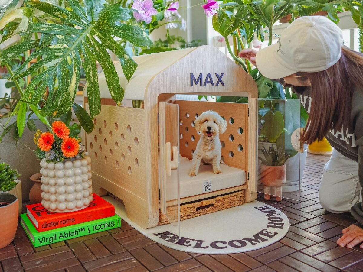 Woman looking at dog in wooden kennel surrounded by plants.