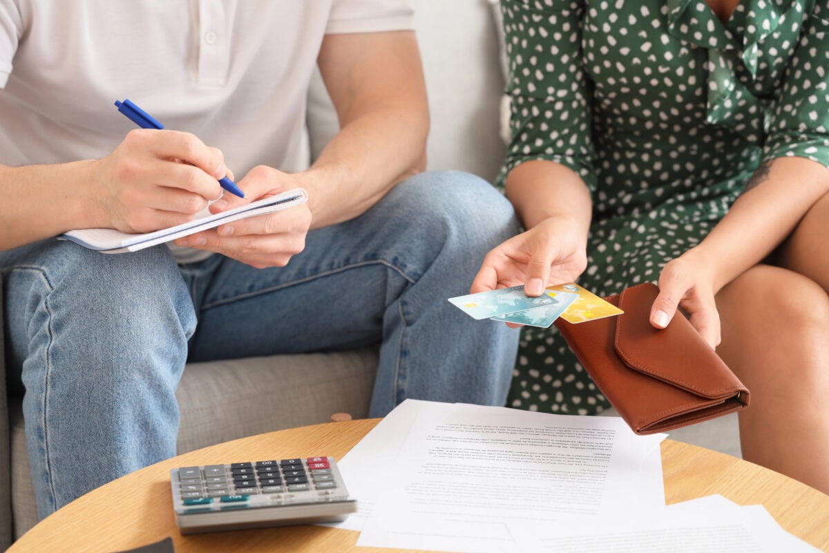Young woman holding credit cards and husband writing down expenses and savings.