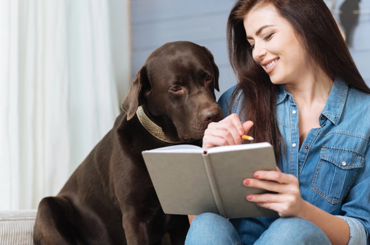 Happy brunette laughing at her pet dog while looking at a schedule. 