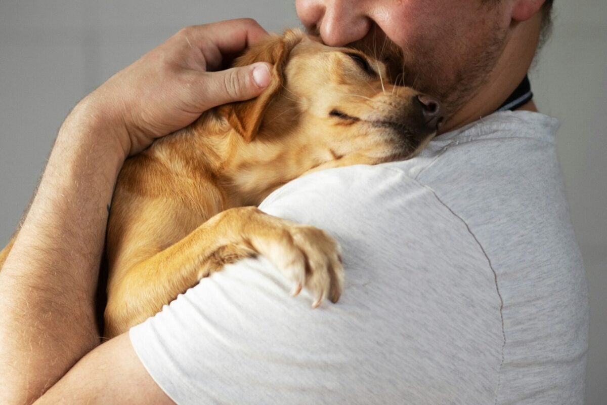 Man holding small dog while dog lays head on man's shoulder.