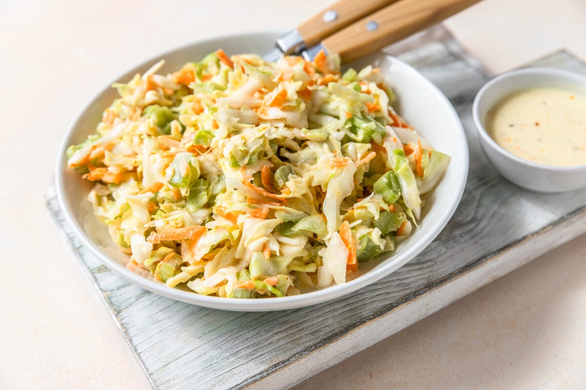 Coleslaw. Salad made of shredded white cabbage, grated carrot and rhubarb with orange mayonnaise dressing in white bowl, light concrete background.