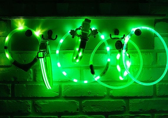 7 Different Green LED Dog Collars hanging up being tested for brightness
