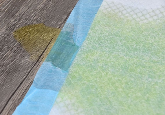 A dog pee pad that has leaks allowing urine to flow onto the floor