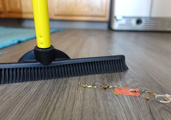 Close up on pile of crumbs, rubbish and dog hair being swept up by rubber-bristled broom