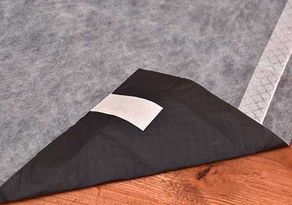 Corner of Bulldogology Carbon Tech Training Pad Folded over to reveal sticky tabs on plastic liner - winner of best premium pee pad for dogs