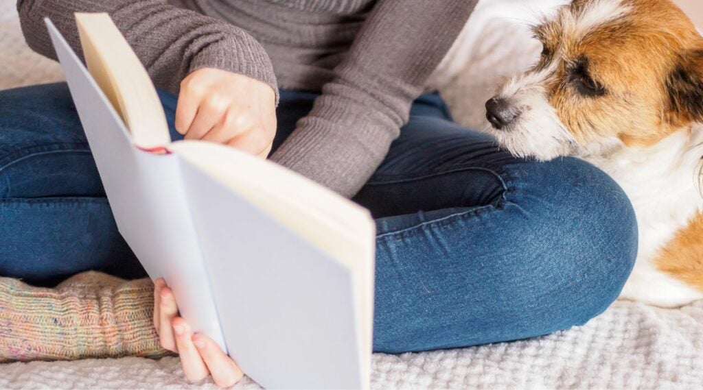 Dog sitting with girl as she reads a book, illustrating good dogs for autistic children.