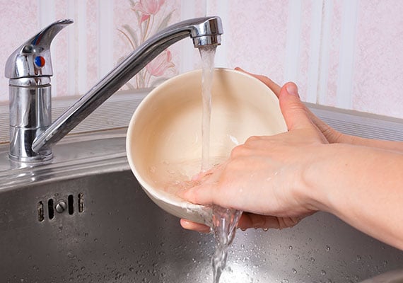 Hand washing a ceramic dog bowl in sink under running water