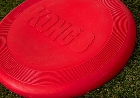 Kong Flyer Red Rubber Frisbee Sitting on grass.