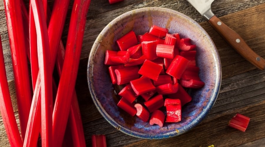 Rhubarb stalks with chopped pieces in a bowl next to it.