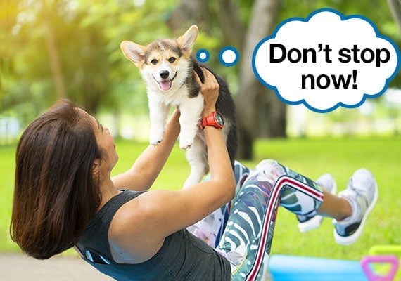 Woman doing abdominal crunch exercise while holding a corgi dog for extra weight