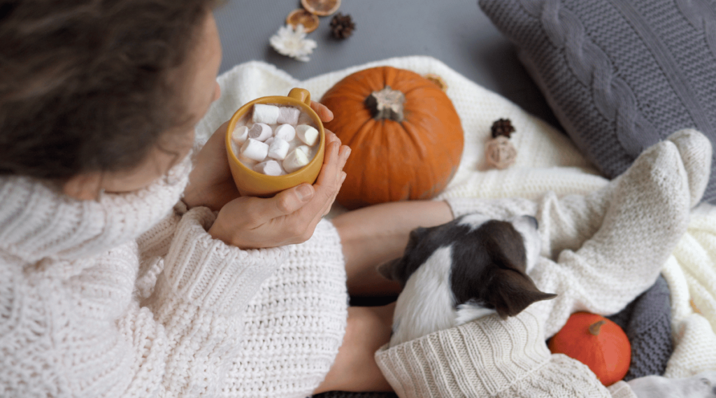 Woman laying with dog holding hot drink with marshmallows