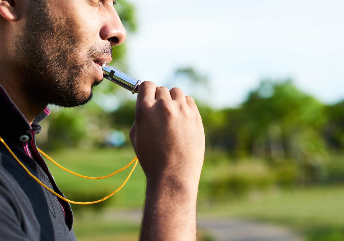 Blowing a dog whistle while hiking through a field.