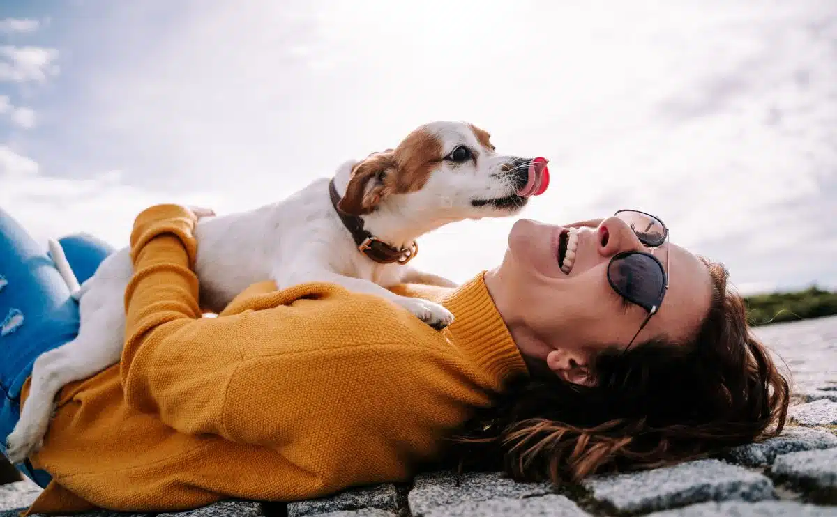 dog licking a girl laying on her back outside