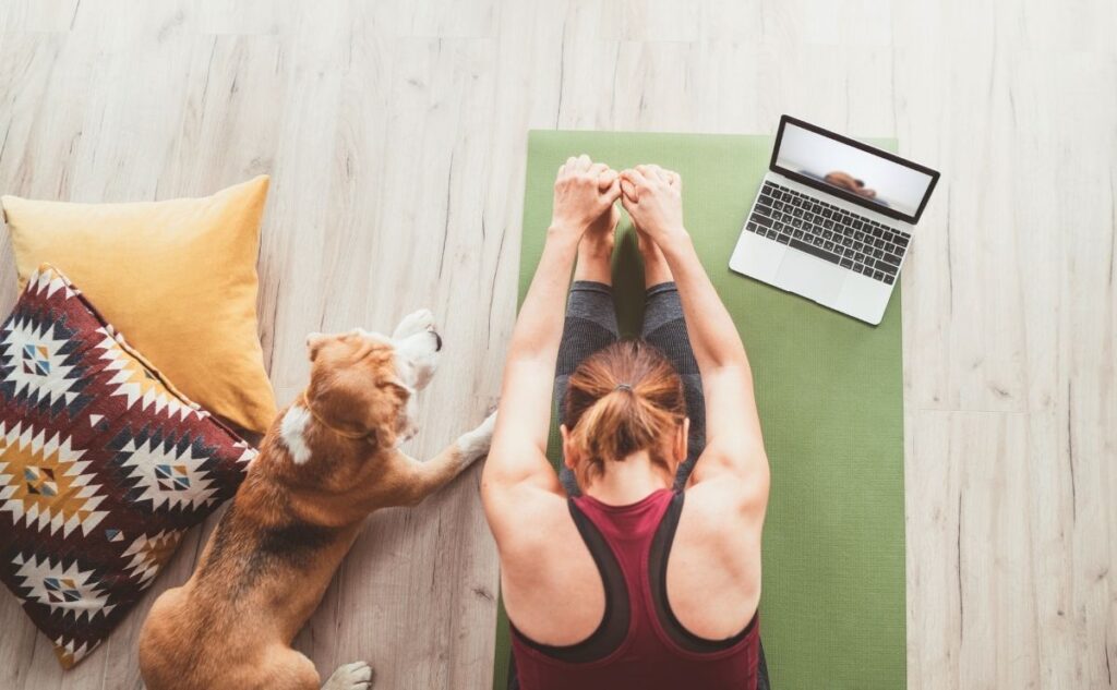 Girl stretching on yoga mat with dog.