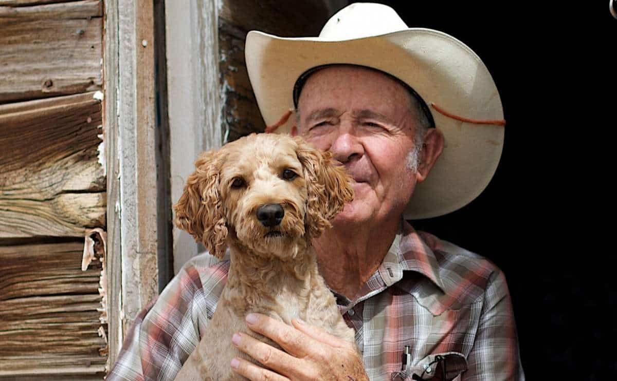 old man with a cowboy hat on holding a dog on a texas ranch