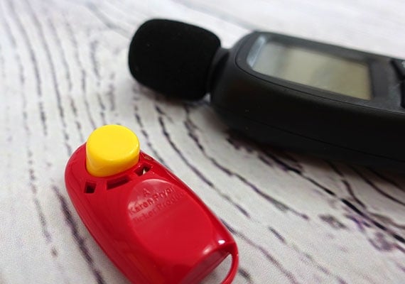 Red dog training clicker sitting on floor next to sound meter to measure decibels
