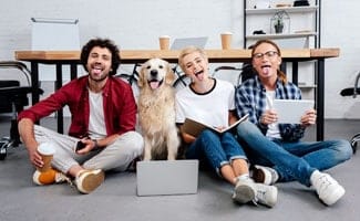 Three business colleagues and a dog sitting in front of a wooden conference table with their tongues out