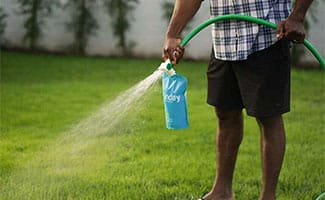 Man spraying Sunday Lawn Care on grass with hose