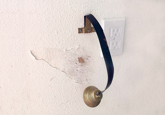 Wall behind dog doorbell that has been scratched by dog paws causing paint to peel with scuff marks