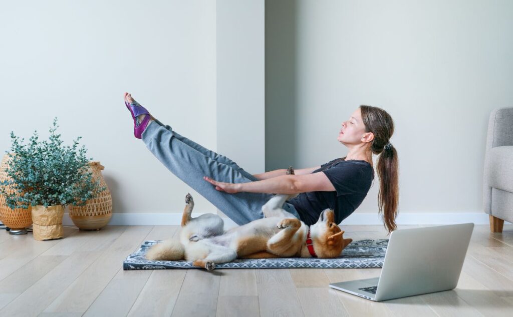 Woman doing boat pose yoga with dog.