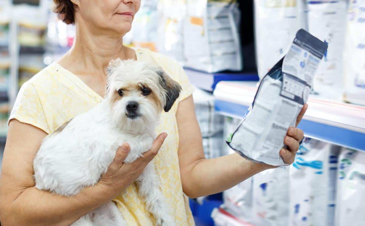 woman looking at dog food bag in pet store holding dog in other arm