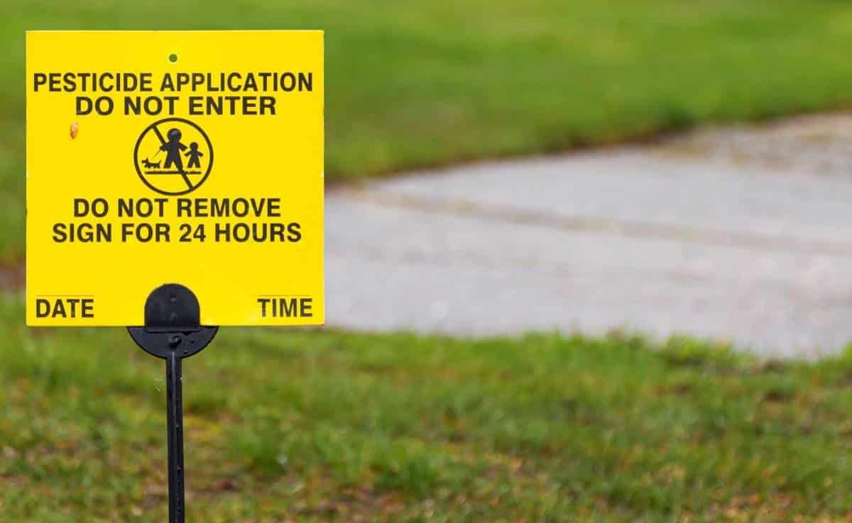 A yellow sign place on a residential lawn reads Pesticide application, do not enter for 24 hours.