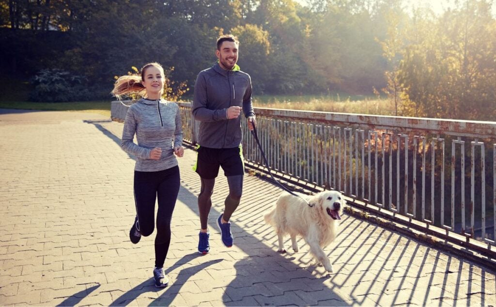 Young couple jogging outside with dog on leash.
